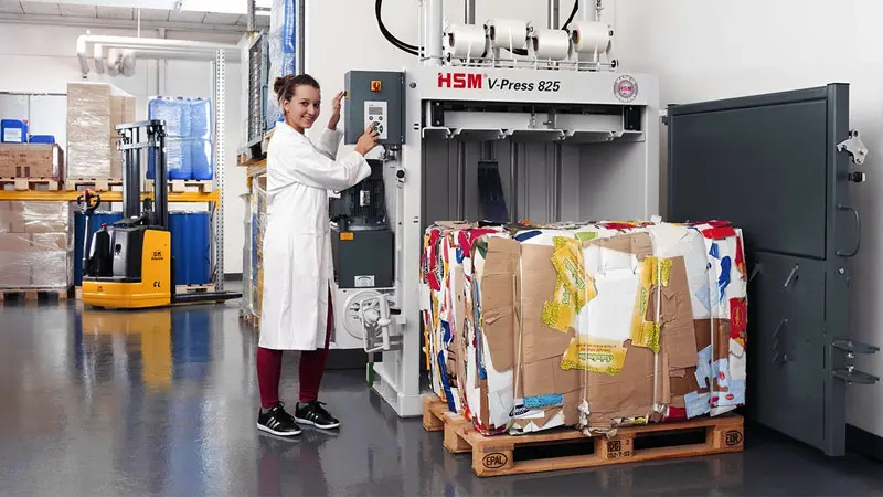 Las prensas compactadoras reducen el volumen del residuo para ahorrar espacio y costes Mujer extrayendo una bala de cartón prensado a un palet con una prensa compactadora